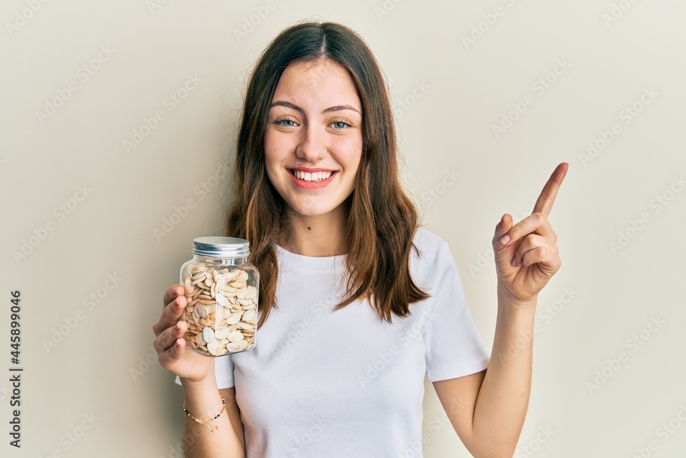 Young brunette woman holding pumpkin seeds smiling happy pointing with hand and finger to the side Young brunette woman holding pumpkin seeds smiling happy pointing with hand and finger to the side