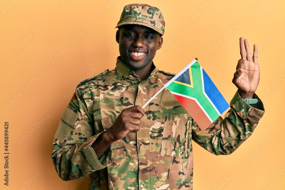Fototapeta premium Young african american man wearing army uniform holding south africa flag doing ok sign with fingers, smiling friendly gesturing excellent symbol