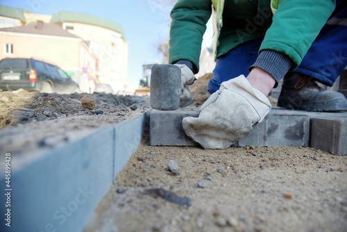 A worker in mittens lays paving slabs on the sand in even rows, builds a pedestrian road.
