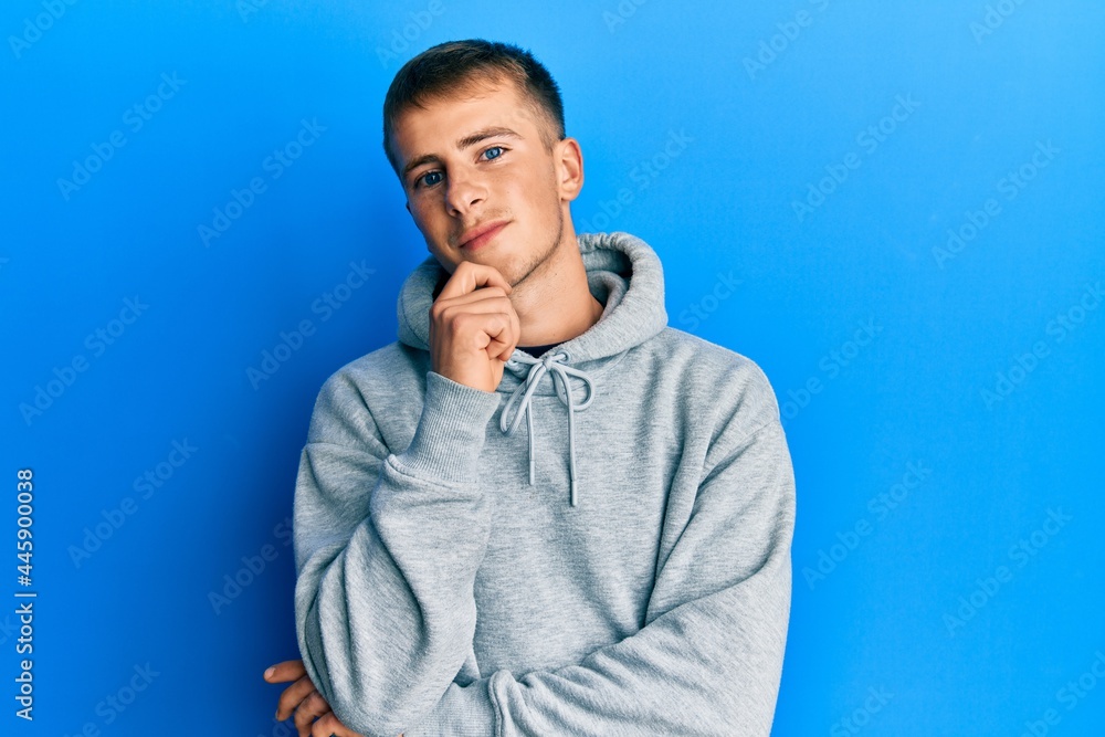 Young caucasian man wearing casual sweatshirt smiling looking confident at the camera with crossed arms and hand on chin. thinking positive. Young caucasian man wearing casual sweatshirt smiling looking confident at the camera with crossed arms and hand on chin. thinking positive.