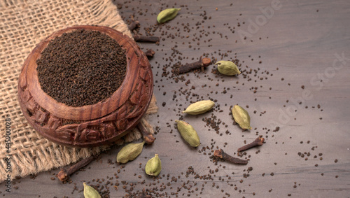 Black Tea Powder or dry dust tea powder, chai patti isolated in wooden bowl with Cardamom, Clove and Ginger.