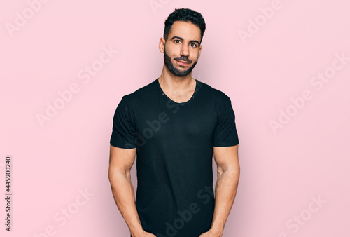 Hispanic man with beard wearing casual black t shirt puffing cheeks with funny face. mouth inflated with air, crazy expression.