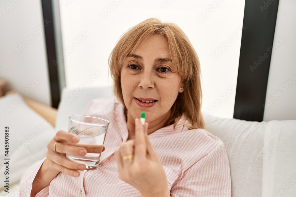Middle age blonde woman illness taking pill lying on the bed at home. Middle age blonde woman illness taking pill lying on the bed at home.