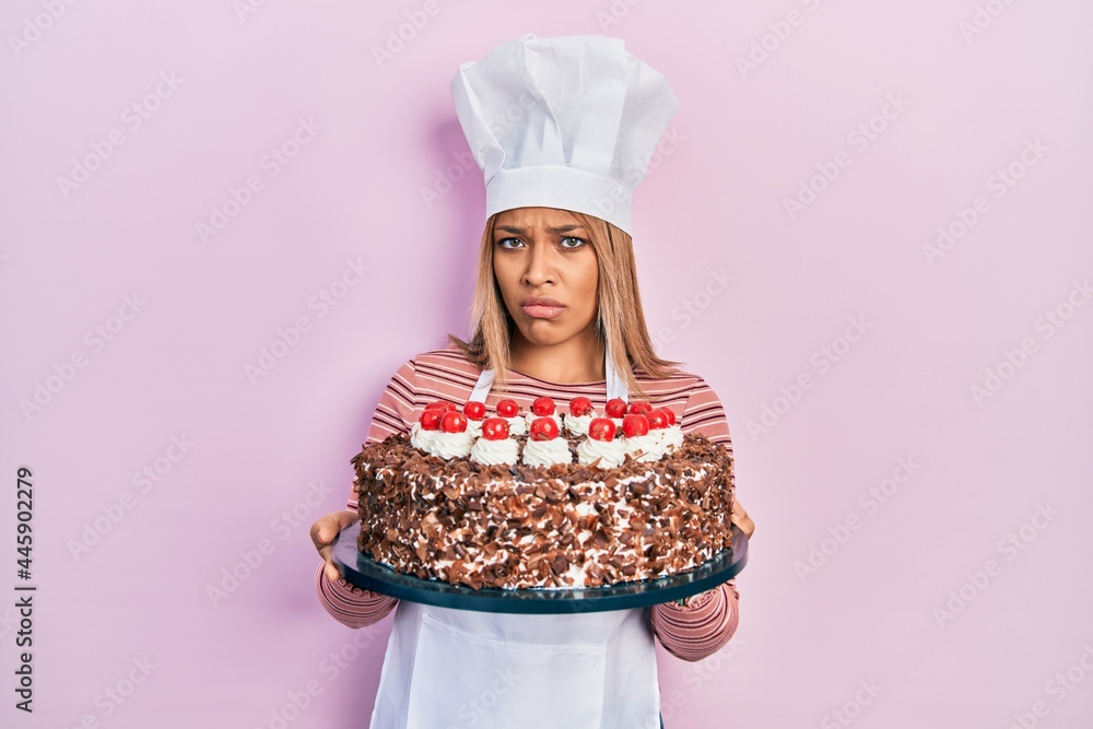 Beautiful hispanic woman wearing cook uniform and hat and birthday cake clueless and confused expression. doubt concept. Beautiful hispanic woman wearing cook uniform and hat and birthday cake clueless and confused expression. doubt concept.