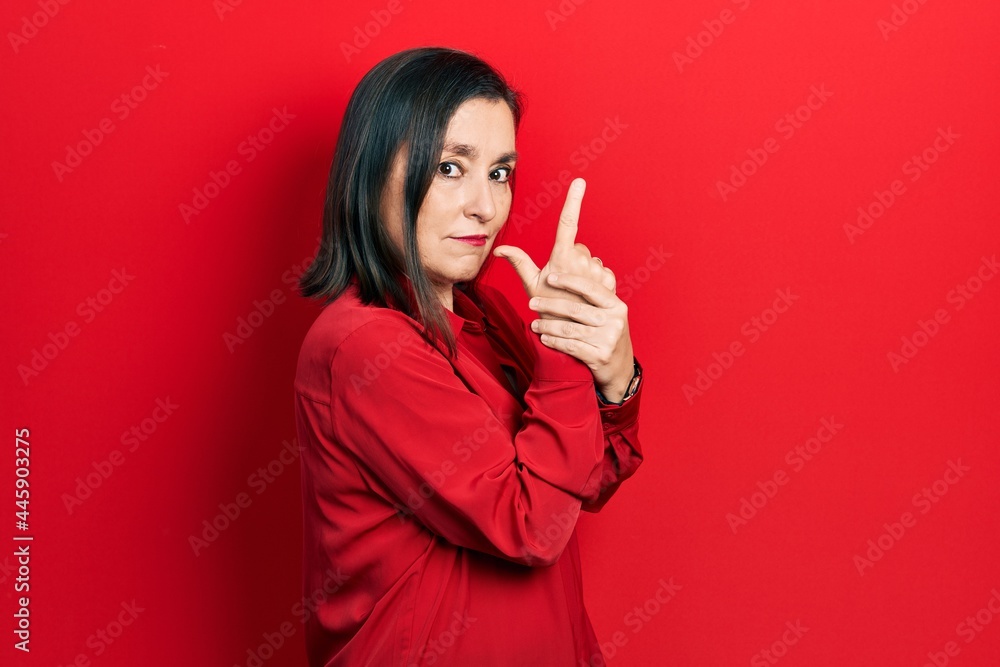 Middle age hispanic woman wearing casual clothes holding symbolic gun with hand gesture, playing killing shooting weapons, angry face Middle age hispanic woman wearing casual clothes holding symbolic gun with hand gesture, playing killing shooting weapons, angry face