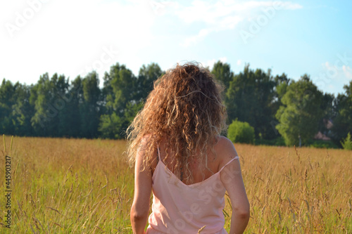 Fototapeta Naklejka Na Ścianę i Meble -  a young girl with long red curly hair walks across the field