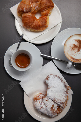 Traditional Italian breakfast. Fresh croissants with cream and sugar powder, espresso coffee and cappuccino on a black wooden table in Milan, Lombardy, Italy. European food and pastry.