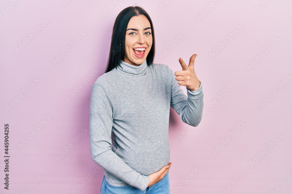 Beautiful woman with blue eyes expecting a baby, touching pregnant belly pointing fingers to camera with happy and funny face. good energy and vibes. Beautiful woman with blue eyes expecting a baby, touching pregnant belly pointing fingers to camera with happy and funny face. good energy and vibes.