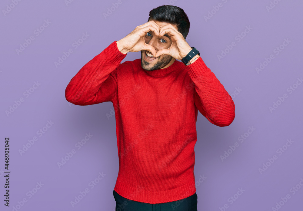 Young hispanic man wearing casual clothes doing heart shape with hand and fingers smiling looking through sign Young hispanic man wearing casual clothes doing heart shape with hand and fingers smiling looking through sign