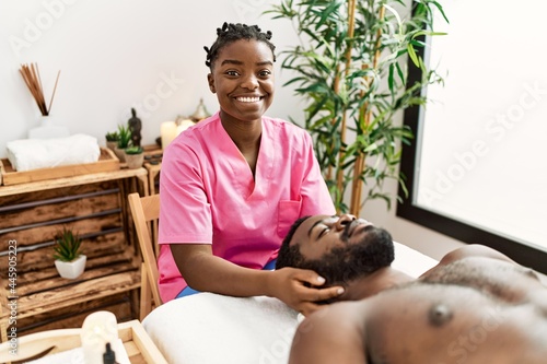 Young physiotherapist woman giving head massage to african american man at the clinic.