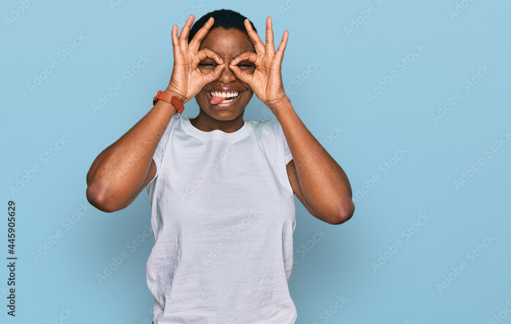 Young african american woman wearing casual white t shirt doing ok gesture like binoculars sticking tongue out, eyes looking through fingers. crazy expression. Young african american woman wearing casual white t shirt doing ok gesture like binoculars sticking tongue out, eyes looking through fingers. crazy expression.