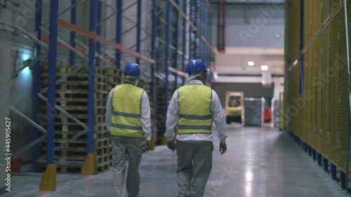 Factory workers walk through large warehouse filled with crates. 