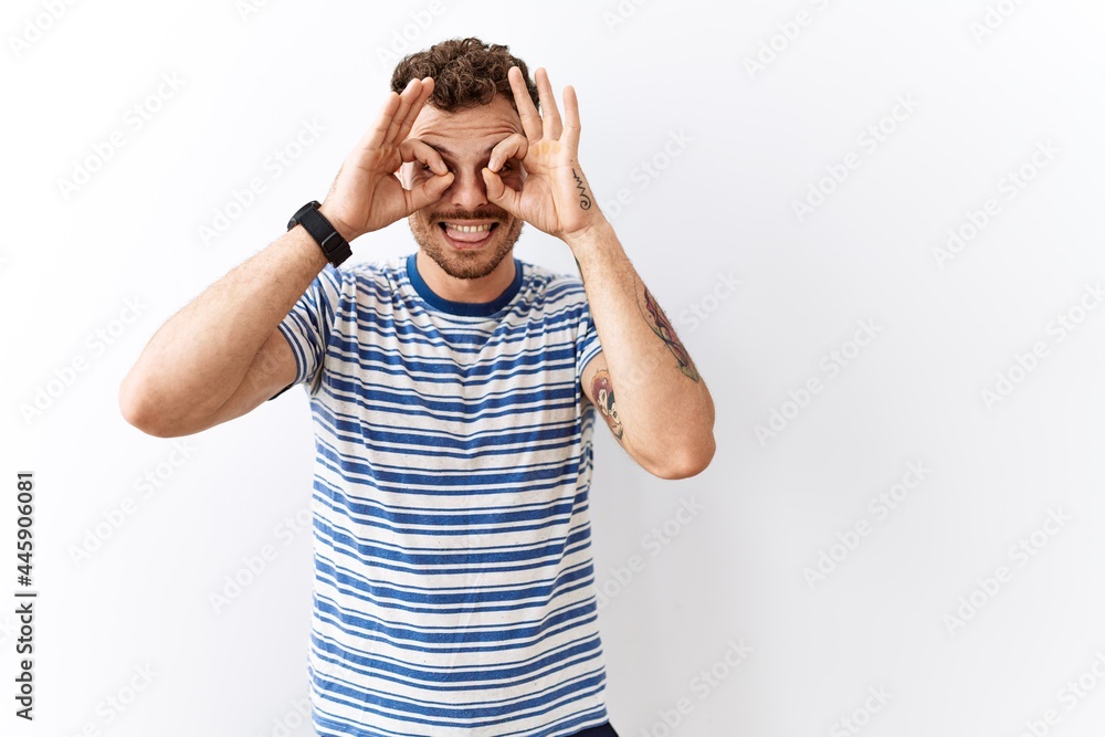Handsome young man standing over isolated background doing ok gesture like binoculars sticking tongue out, eyes looking through fingers. crazy expression. Handsome young man standing over isolated background doing ok gesture like binoculars sticking tongue out, eyes looking through fingers. crazy expression.