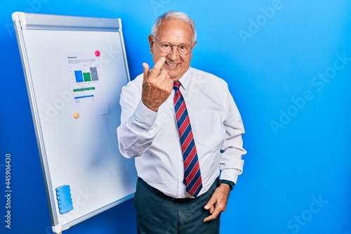 Senior man with grey hair standing by business blackboard beckoning come here gesture with hand inviting welcoming happy and smiling