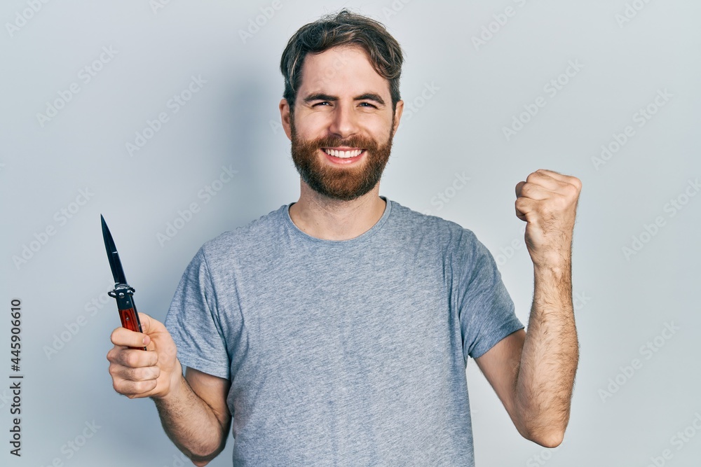 Caucasian man with beard holding pocket knife screaming proud, celebrating victory and success very excited with raised arms Caucasian man with beard holding pocket knife screaming proud, celebrating victory and success very excited with raised arms