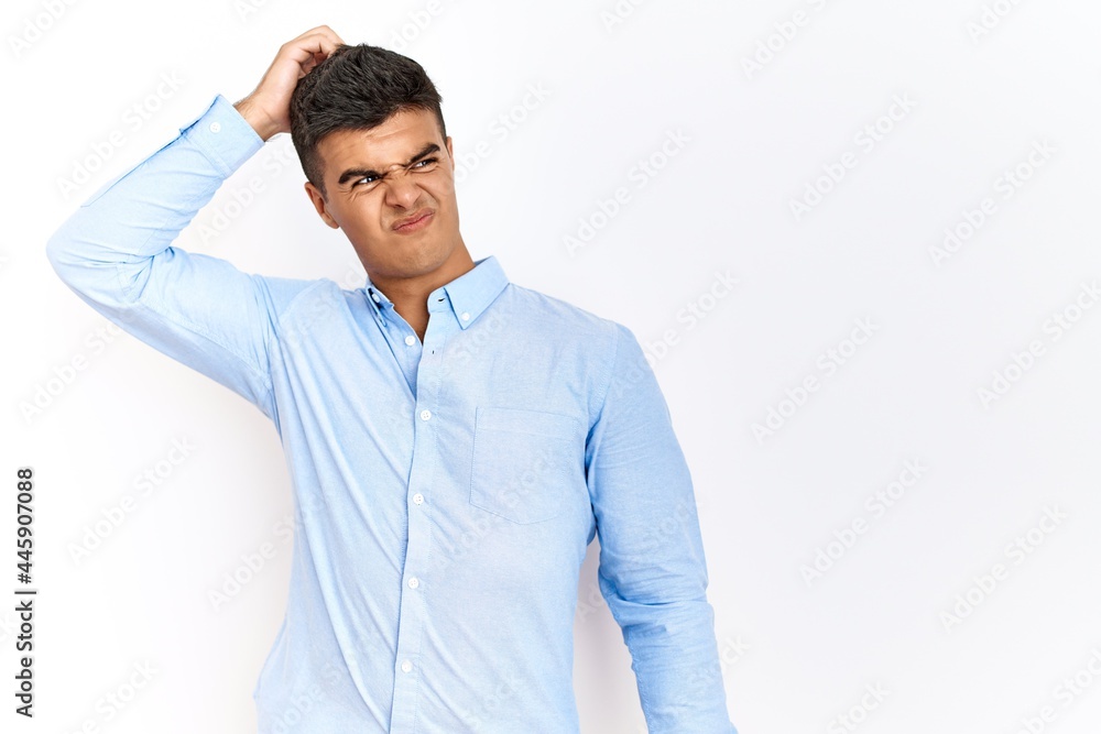 Young hispanic man wearing business shirt standing over isolated background confuse and wondering about question. uncertain with doubt, thinking with hand on head. pensive concept. Young hispanic man wearing business shirt standing over isolated background confuse and wondering about question. uncertain with doubt, thinking with hand on head. pensive concept.