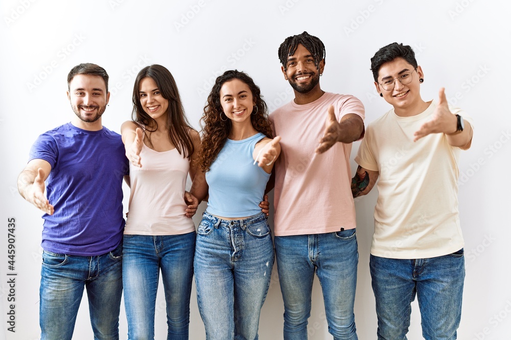 Group of young people standing together over isolated background smiling friendly offering handshake as greeting and welcoming. successful business. Group of young people standing together over isolated background smiling friendly offering handshake as greeting and welcoming. successful business.