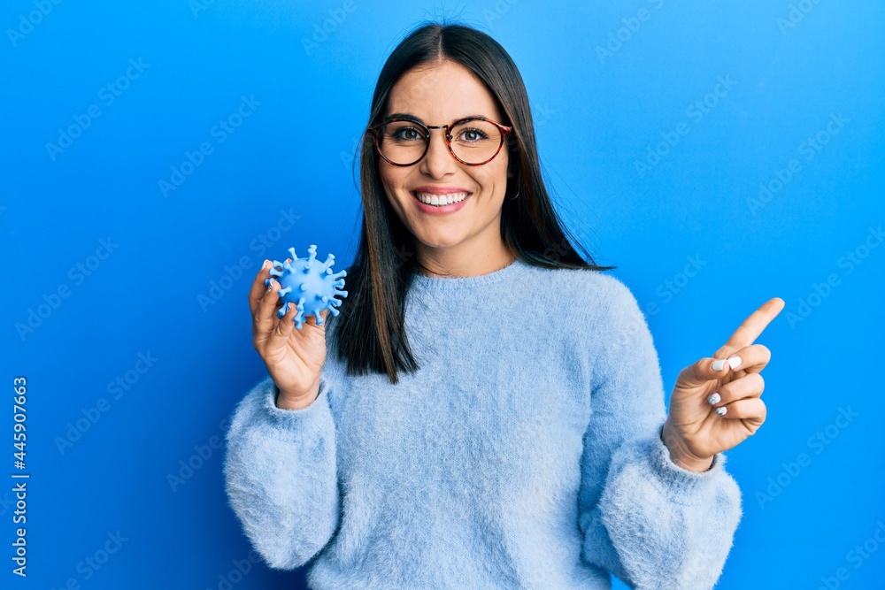 Young brunette woman holding virus toy smiling happy pointing with hand and finger to the side Young brunette woman holding virus toy smiling happy pointing with hand and finger to the side