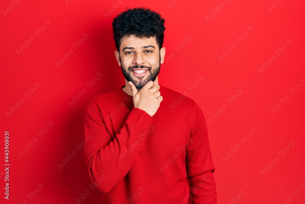 Young arab man with beard wearing casual red sweater looking confident at the camera smiling with crossed arms and hand raised on chin. thinking positive. Young arab man with beard wearing casual red sweater looking confident at the camera smiling with crossed arms and hand raised on chin. thinking positive.