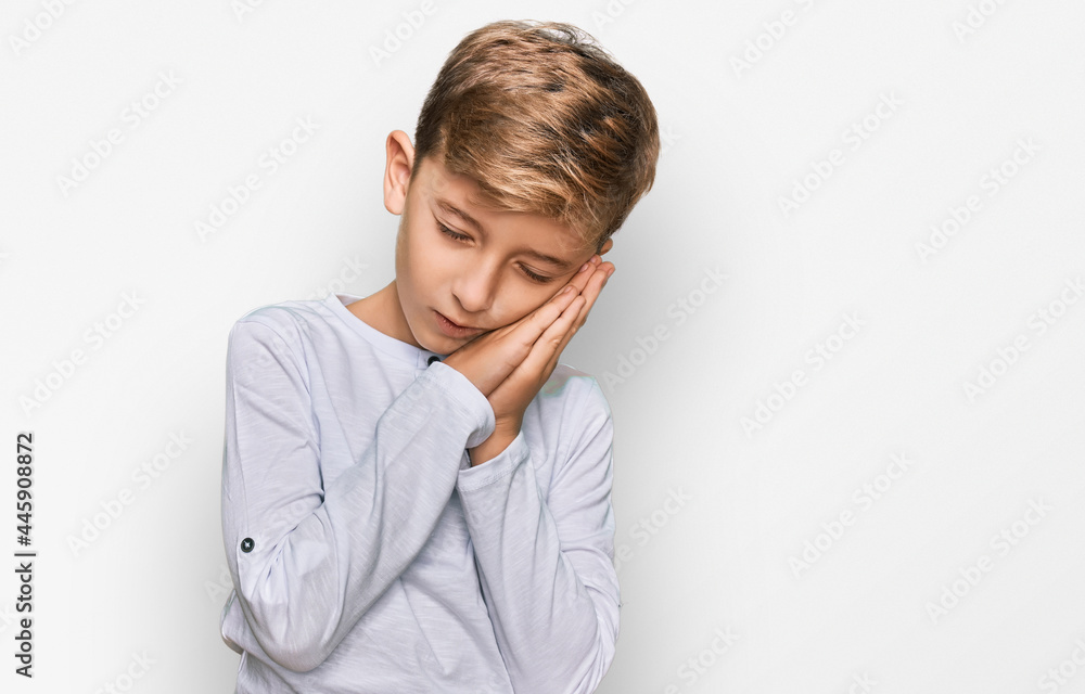 Little caucasian boy kid wearing casual clothes sleeping tired dreaming and posing with hands together while smiling with closed eyes.