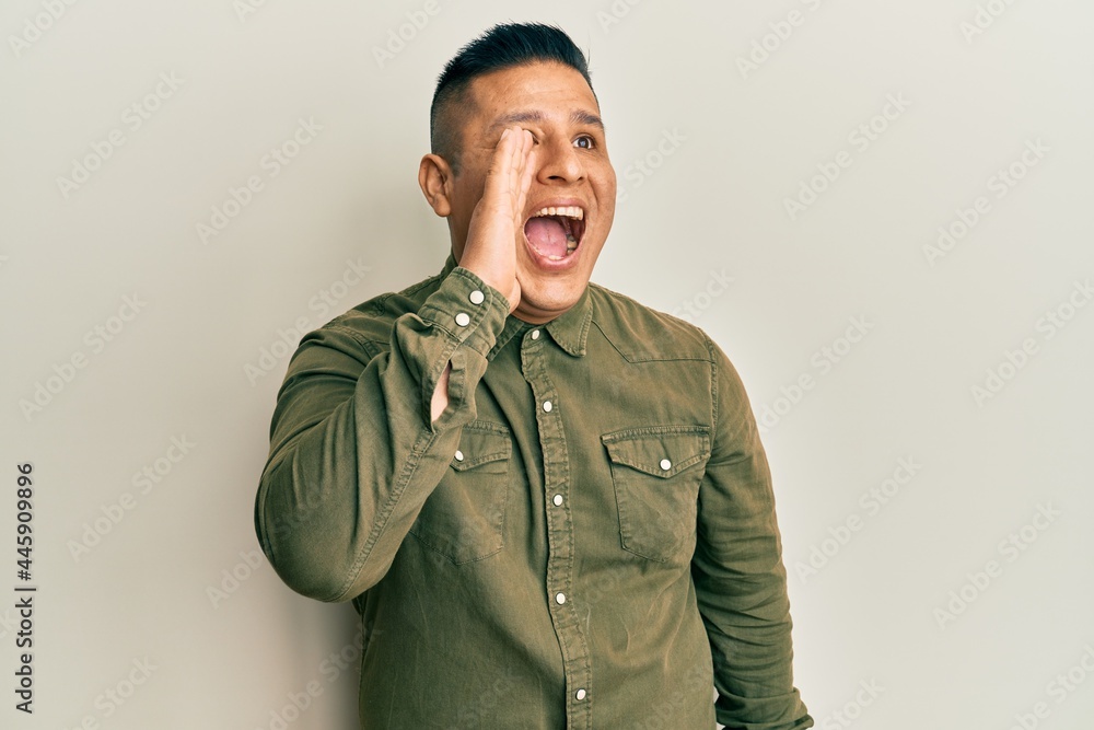 Young latin man wearing casual clothes shouting and screaming loud to side with hand on mouth. communication concept. Young latin man wearing casual clothes shouting and screaming loud to side with hand on mouth. communication concept.
