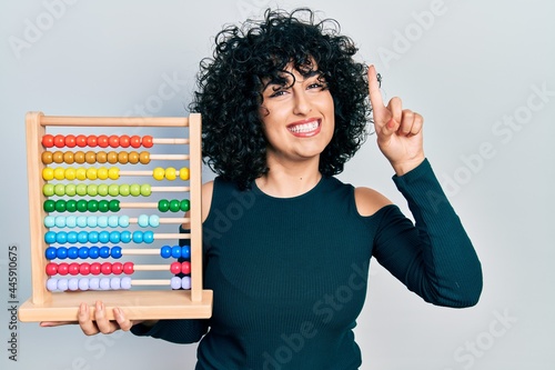 Young middle east woman holding traditional abacus smiling with an idea or question pointing finger with happy face, number one photo