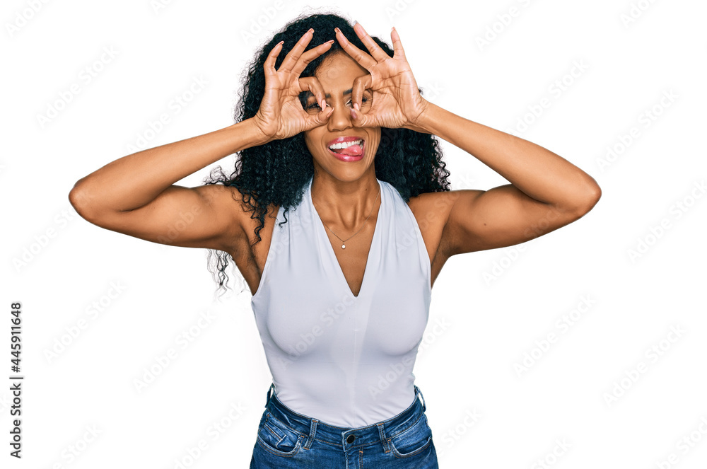 Middle age african american woman wearing casual style with sleeveless shirt doing ok gesture like binoculars sticking tongue out, eyes looking through fingers. crazy expression. Middle age african american woman wearing casual style with sleeveless shirt doing ok gesture like binoculars sticking tongue out, eyes looking through fingers. crazy expression.
