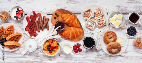 Breakfast or brunch table scene on a white wood banner background. Top view. Variety of sweet and savory food items.