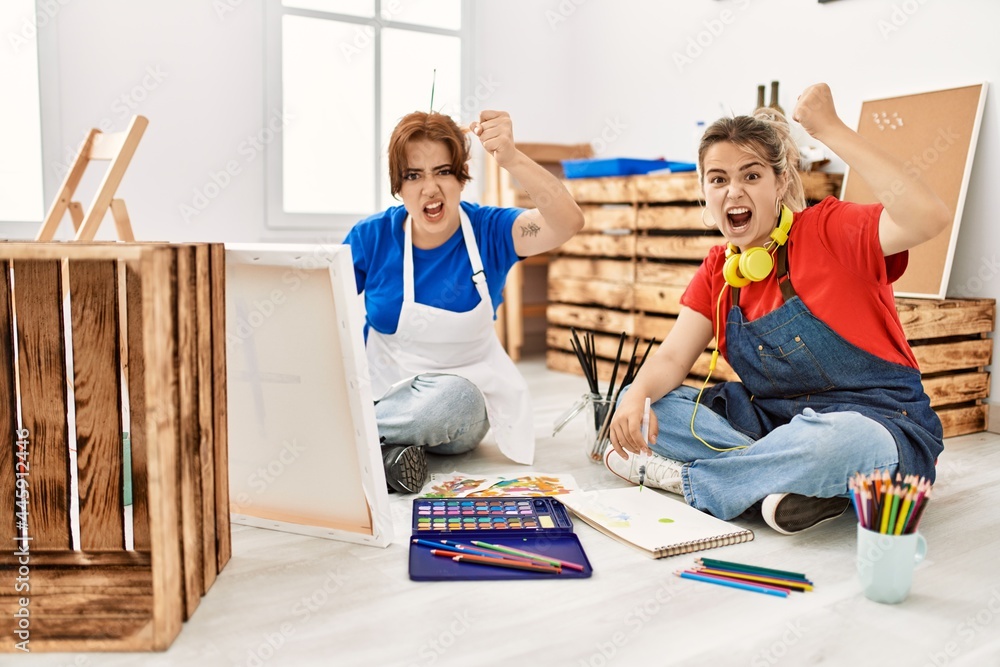 Obraz premium Two beautiful women painting at art studio annoyed and frustrated shouting with anger, yelling crazy with anger and hand raised