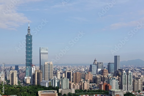 Aerial panorama of Downtown Taipei  vibrant capital city of Taiwan  with prominent Taipei 101 Tower among skyscrapers in Xinyi District   Yangmingshan Mountain on distant horizon under blue sunny sky