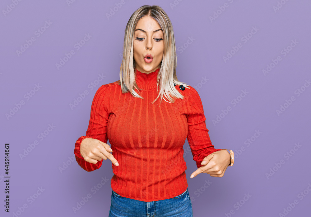 Beautiful blonde woman wearing casual clothes pointing down with fingers showing advertisement, surprised face and open mouth Beautiful blonde woman wearing casual clothes pointing down with fingers showing advertisement, surprised face and open mouth