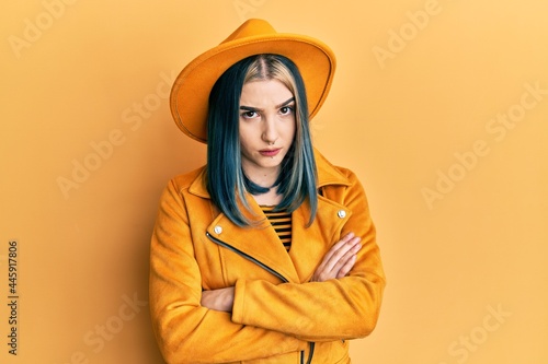 Young modern girl wearing yellow hat and leather jacket skeptic and nervous, disapproving expression on face with crossed arms. negative person.