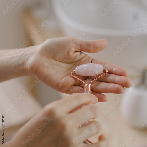 Female holding pink quartz roller for face massage while doing beauty morning routine in bathroom