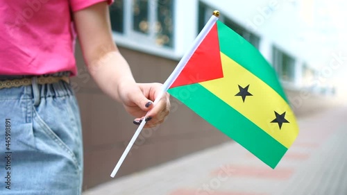 Unrecognizable woman holding Sao Tomean flag. Girl walking down street with national flag of Sao Tome and Principe