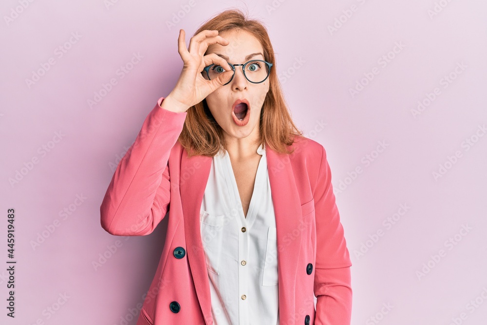 Young caucasian woman wearing business style and glasses doing ok gesture shocked with surprised face, eye looking through fingers. unbelieving expression.
