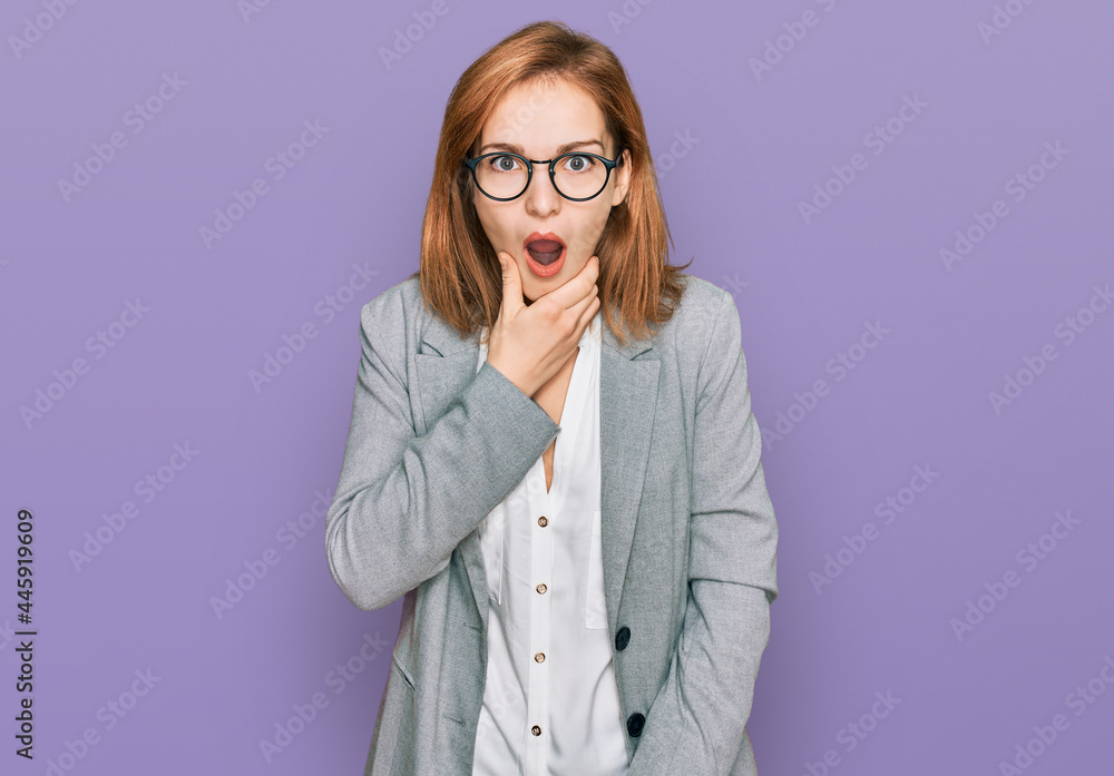 Young caucasian woman wearing business style and glasses looking fascinated with disbelief, surprise and amazed expression with hands on chin