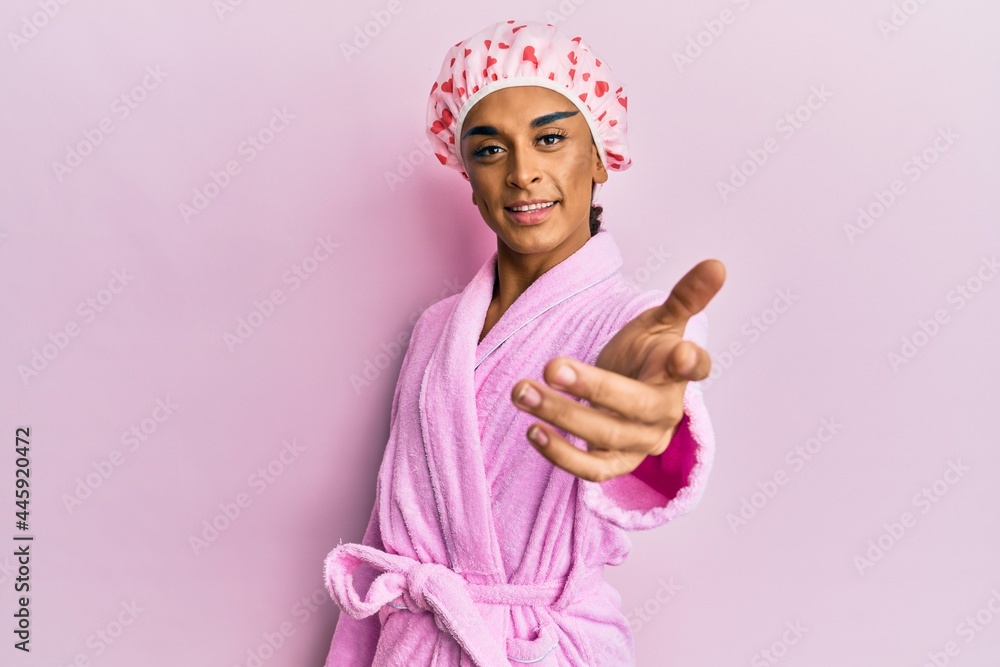 Hispanic man wearing make up wearing shower towel cap and bathrobe smiling friendly offering handshake as greeting and welcoming. successful business. Hispanic man wearing make up wearing shower towel cap and bathrobe smiling friendly offering handshake as greeting and welcoming. successful business.