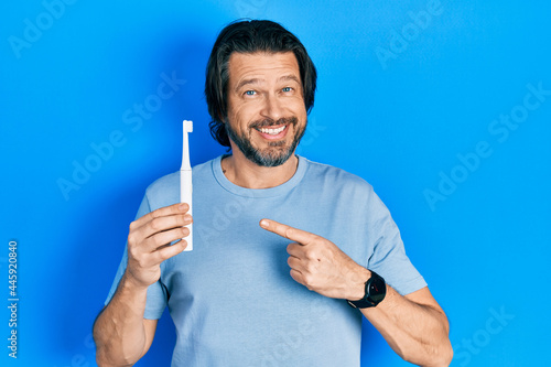 Middle age caucasian man holding electric toothbrush smiling happy pointing with hand and finger