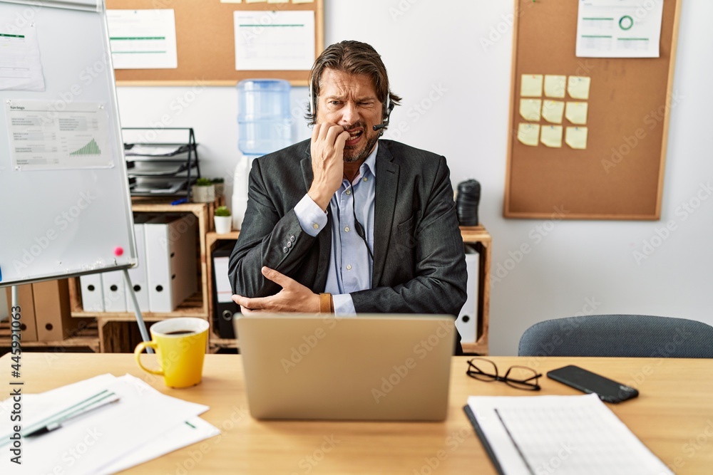 Naklejka premium Handsome middle age man wearing call center agent headset at the office looking stressed and nervous with hands on mouth biting nails. anxiety problem.