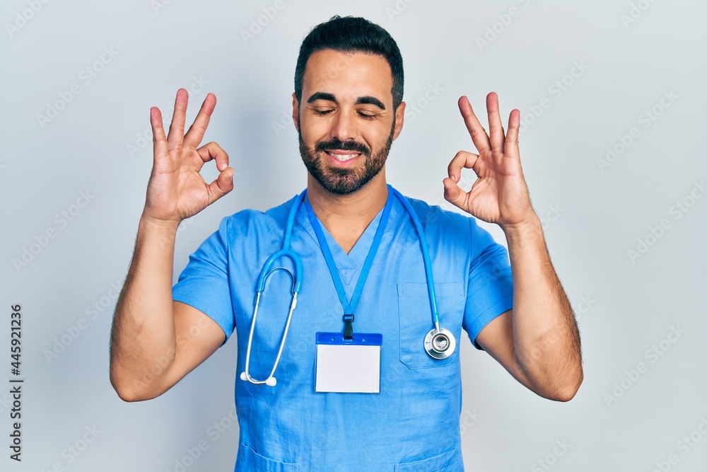 Handsome hispanic man with beard wearing doctor uniform relax and smiling with eyes closed doing meditation gesture with fingers. yoga concept. Handsome hispanic man with beard wearing doctor uniform relax and smiling with eyes closed doing meditation gesture with fingers. yoga concept.