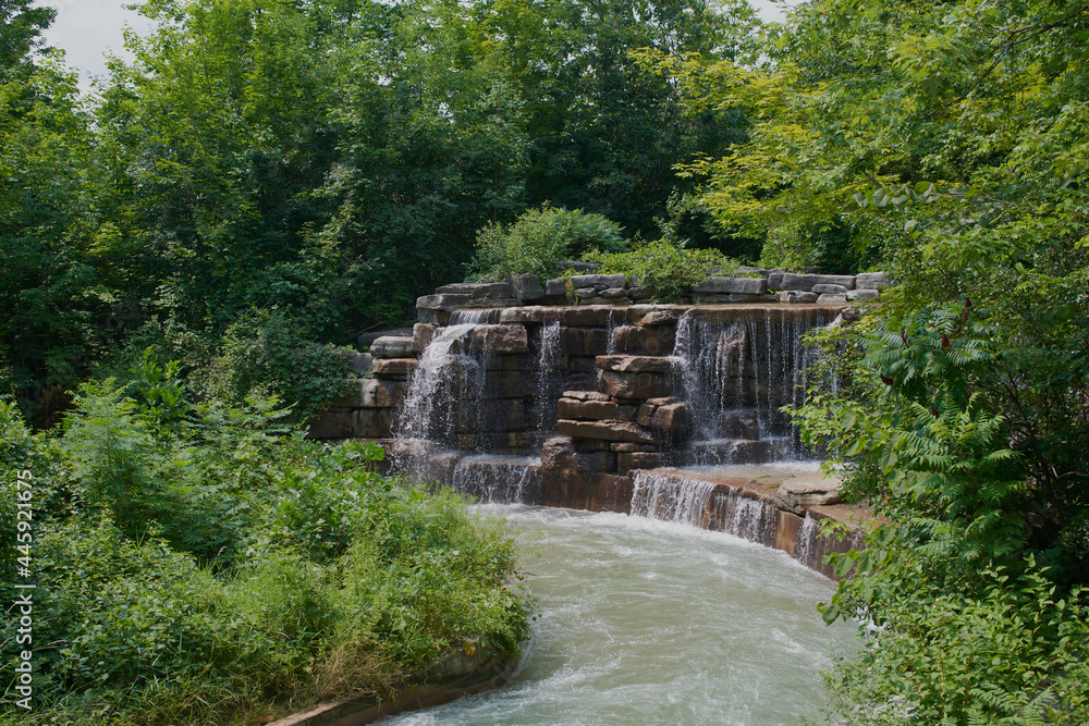 Beautiful colorful summer spring natural landscape with a lake in Park surrounded by green foliage of trees in sunlight and stone path in foreground.