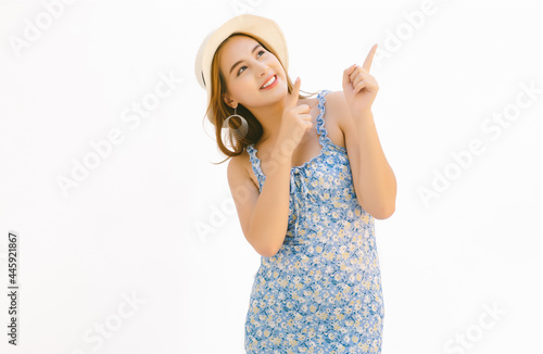 Beautiful young Asian woman dressed in blue floral dress and wearing summer straw hat  pointing fingers up with two hands at copy space isolated over white background. photo