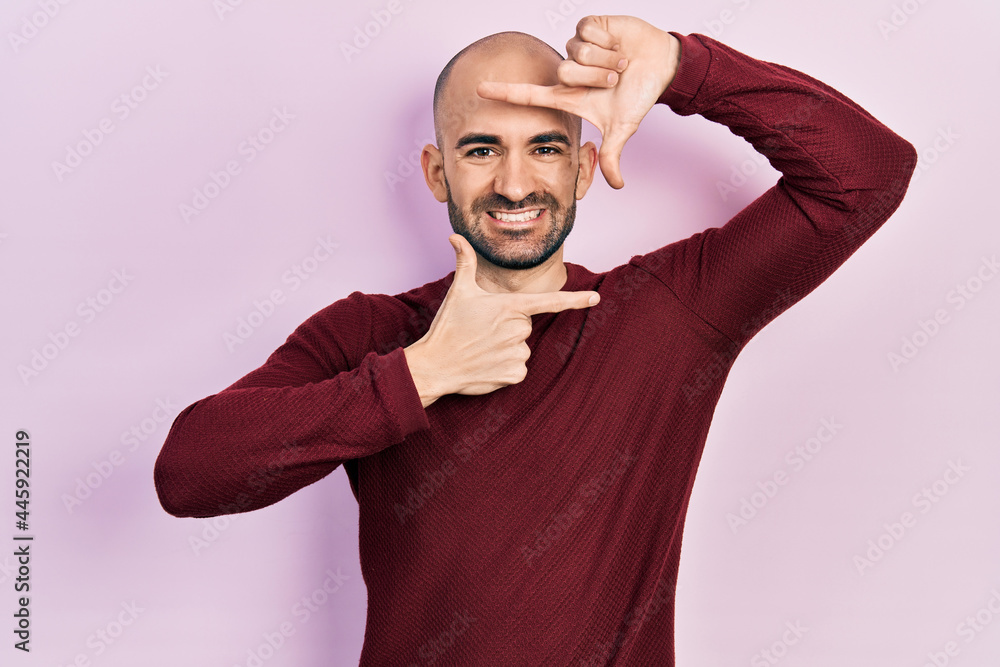 Fototapeta premium Young bald man wearing casual clothes smiling making frame with hands and fingers with happy face. creativity and photography concept.
