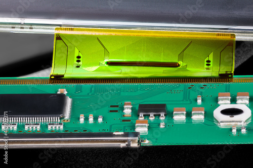 Printed circuit board connected by flexible flat cable to a LCD panel. Closeup of electronic components as micro chip, inductor or capacitor on green PCB and plastic FPC interface for digital display. photo