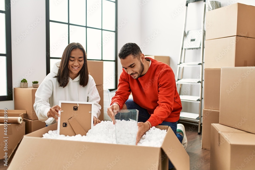 Young latin couple smiling happy unboxing cardboard box at new home. Young latin couple smiling happy unboxing cardboard box at new home.