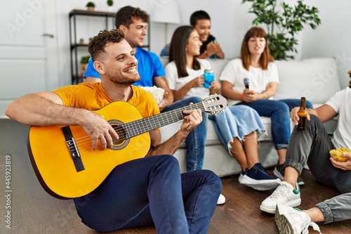 Group of young friends on party smiling happy and playing classical guitar at home.