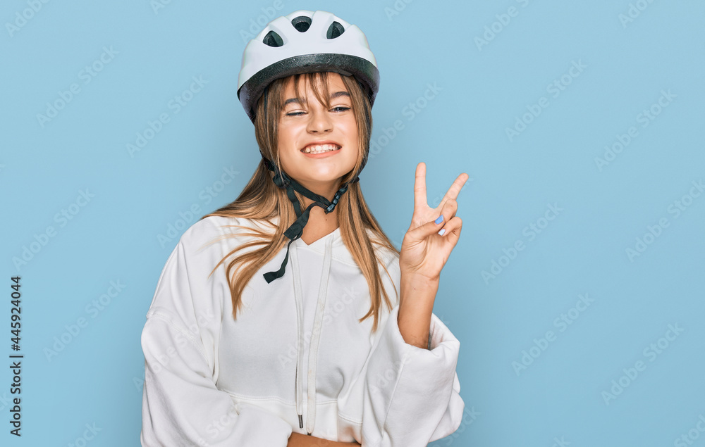 Teenager caucasian girl wearing bike helmet smiling with happy face winking at the camera doing victory sign. number two. Teenager caucasian girl wearing bike helmet smiling with happy face winking at the camera doing victory sign. number two.