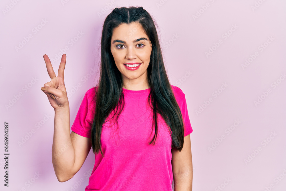 Young hispanic girl wearing casual pink t shirt showing and pointing up with fingers number two while smiling confident and happy.