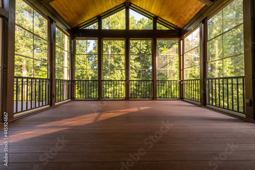 Fototapeta Modern new screened porch with plastic windows and composite floor with summer woods in the background