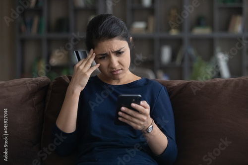 Unhappy young Indian woman distressed with payment problems shopping online from home on smartphone with credit debit card. Upset biracial female buyer frustrated with bank error on cell.